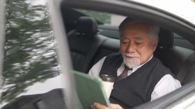 4k亚洲高级商人坐在汽车后座上喝热咖啡，在数字平板电脑上工作