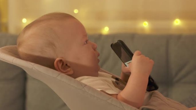 可爱的小孩使用移动设备，男婴在电视上看电影，同时使用智能手机。