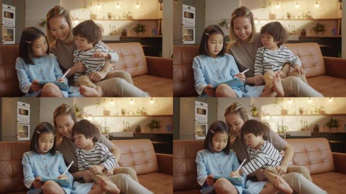 充满爱心的亚洲妈妈和小女儿和儿子一起坐在家里的沙发上，平板电脑设备用铅笔绘制，使用教育应用程序轻松有