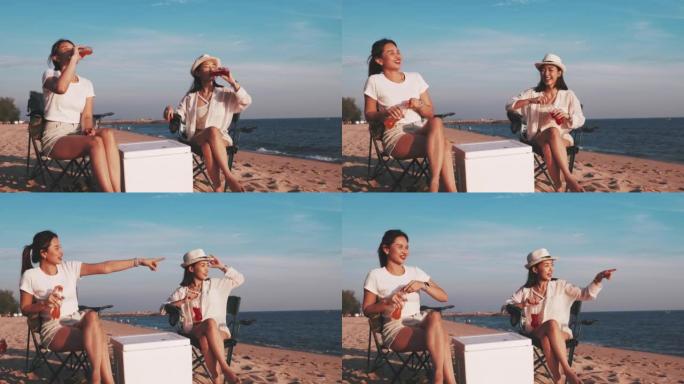 两个十几岁的女孩坐在海滩上碰碰瓶子，喝苏打水，一群朋友在日落时享受饮料和在露营海滩弹吉他，度假和生活