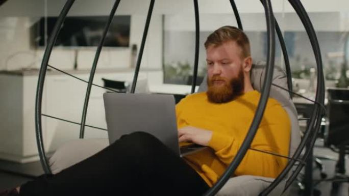 男子在工作场所使用笔记本电脑坐在蛋椅上工作