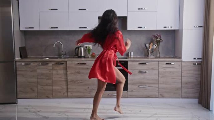 年轻女孩穿着红色性感长袍和黑色内衣，在现代明亮的厨房里穿着漂亮的身体在家里跳舞