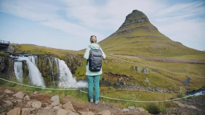 冰岛。女性旅行者早上看绿山峰和柯克朱费尔。夏季冒险之旅
