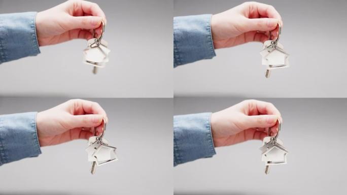 女人的衬衫特写镜头清晰地显示了带有金属钥匙扣的新钥匙。灰色背景。抵押贷款、购买房地产和租赁的概念