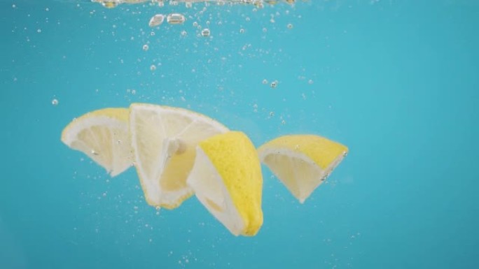 将柠檬片倒入蓝色背景上的水中的慢动作