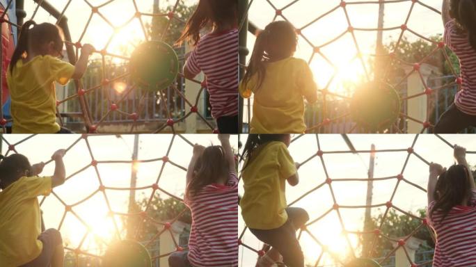 快乐的两个小女孩在操场上爬绳网。户外操场上活跃的小女孩。儿童健康暑期活动。
