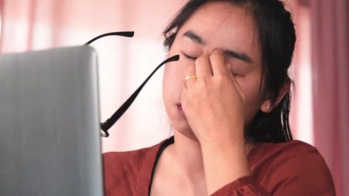 在家里长时间在笔记本电脑上工作后，认真的亚洲妇女感到疲倦和眼睛疲劳。健康和办公室综合症概念。