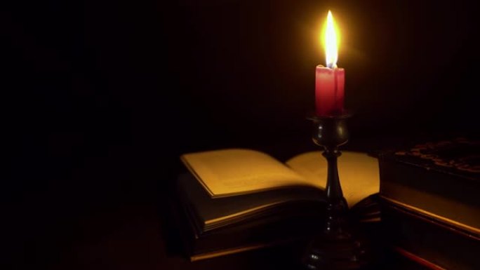 带有燃烧的蜡烛存根照亮一本打开的书的泥水烛台的黑暗神秘图像