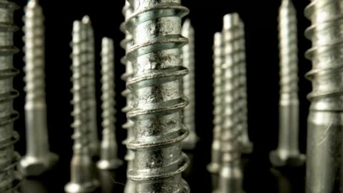 金属螺钉、不锈钢螺栓、带螺纹的钢锚在黑色背景上旋转。螺旋建筑材料，用于修理、固定、拧紧。特写。慢动作