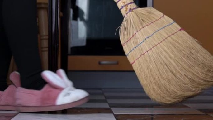 年轻女孩用普通的扫帚在厨房里扫地板