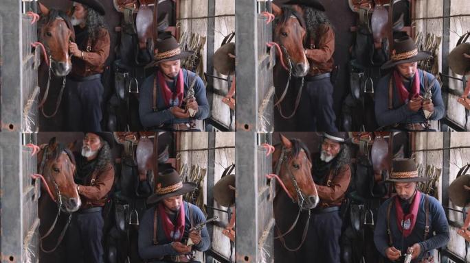 两个穿着牛仔服装的男人呆在马stable里，一个检查短枪的子弹，另一个在后面照顾马