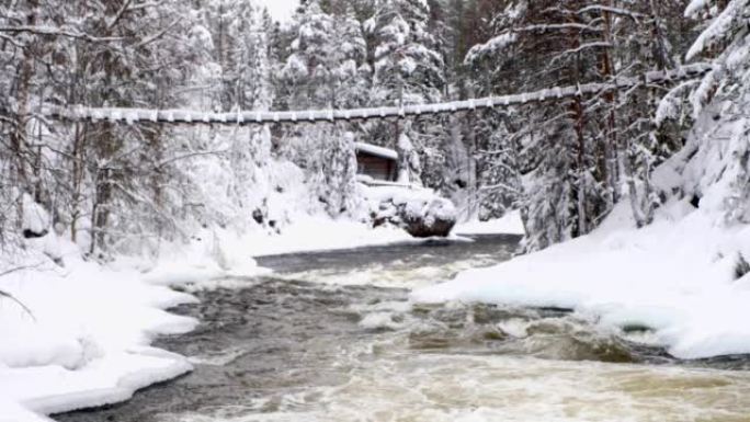 有河海岸线的白雪皑皑的风景。冰雪覆盖的森林和吊桥以及河流急流。