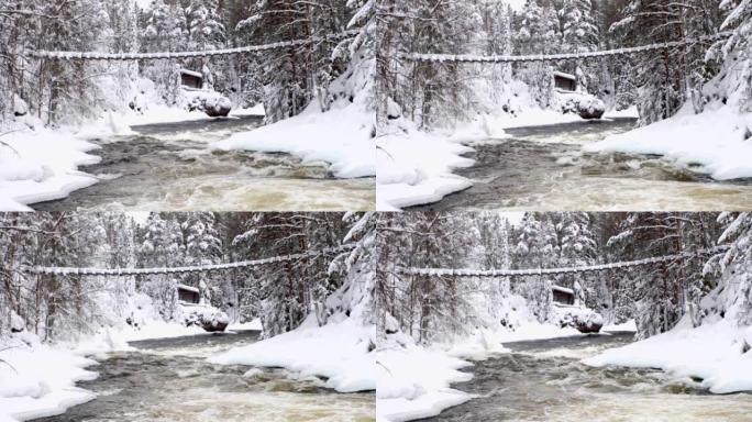 有河海岸线的白雪皑皑的风景。冰雪覆盖的森林和吊桥以及河流急流。