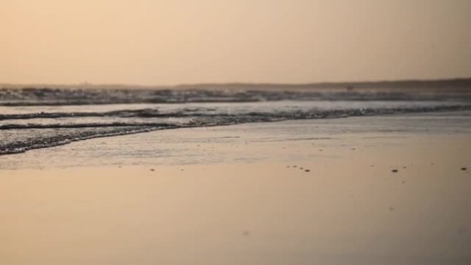 日落时岸上平静海滩波浪的低角度拍摄。晚上舒缓的海洋和橙色的天空。轻松的暑假背景。去自然之地旅行