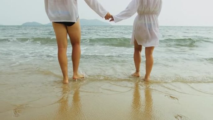 可爱的情侣穿着白色连衣裙一起在海里游泳。女人和男人走路，牵手