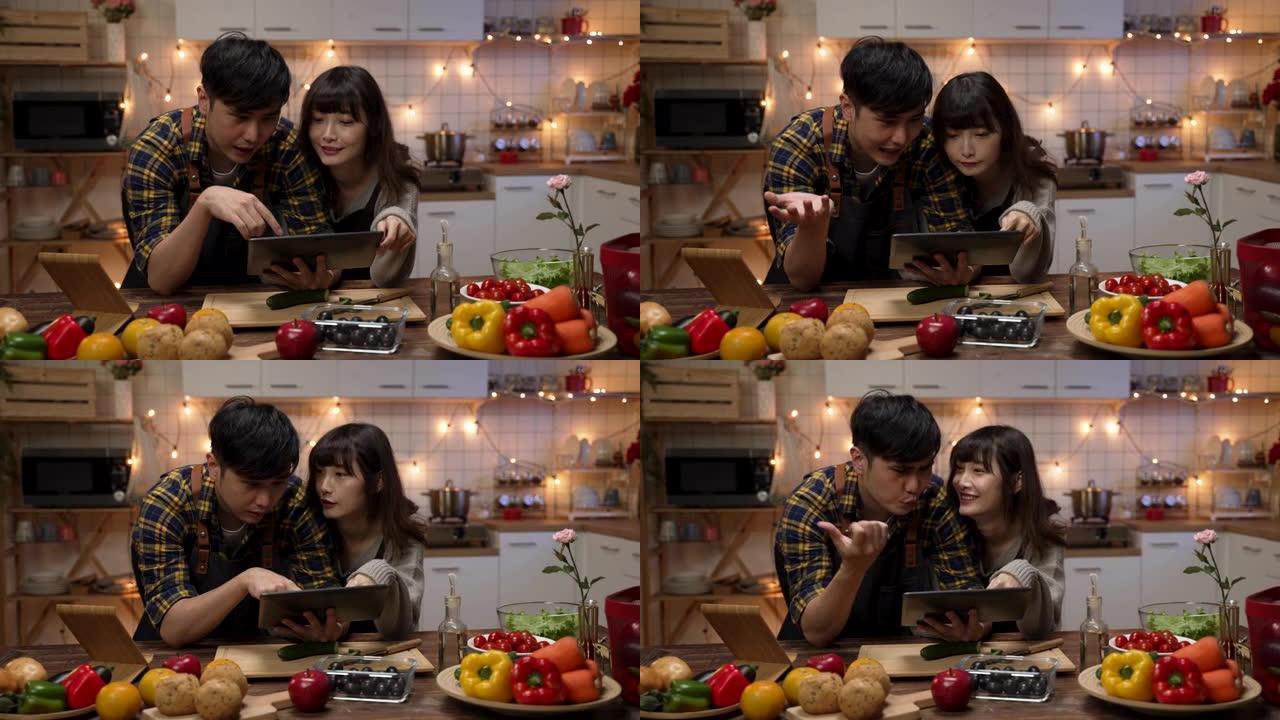快乐的亚洲情侣在家里的厨房里一起计划和决定情人节晚餐食谱时，使用触摸板