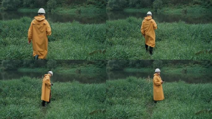戴着头盔和雨衣的工人走到草地上的河边，男人手里拿着电话