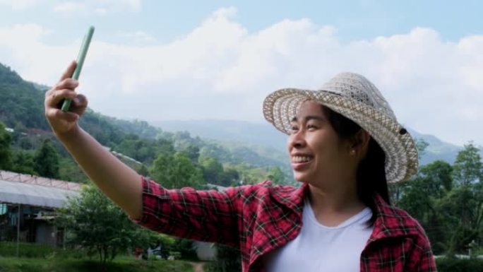 戴着帽子的时髦女人在度假时在大自然中放松，并在山地背景下用智能手机自拍。
