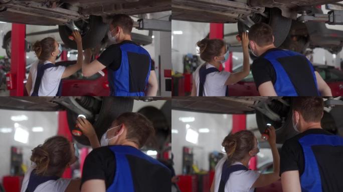 女机械师检查汽车悬架。强壮的女人执教一名男性实习生。工人在升降机上检查车辆的底部和行驶装置。因检疫限