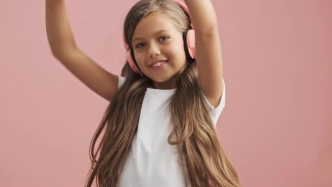快乐的小女孩戴着粉色耳机听音乐跳舞
