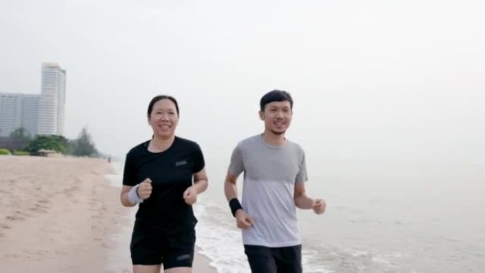 4K 25fps慢动作，这对年轻的亚洲夫妇，早晨一起在寒风中慢跑，天气凉爽宜人，海浪在奔跑时打在他们