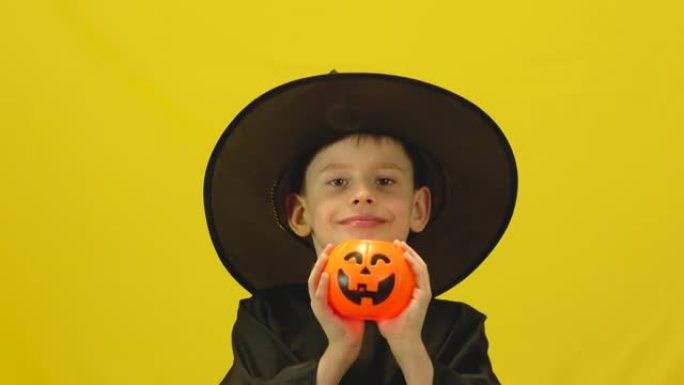 开朗的白人儿童7岁，穿着化装舞会神秘服装，戴着一顶帽子，手持南瓜灯庆祝万圣节。儿童和传统的万圣节假期