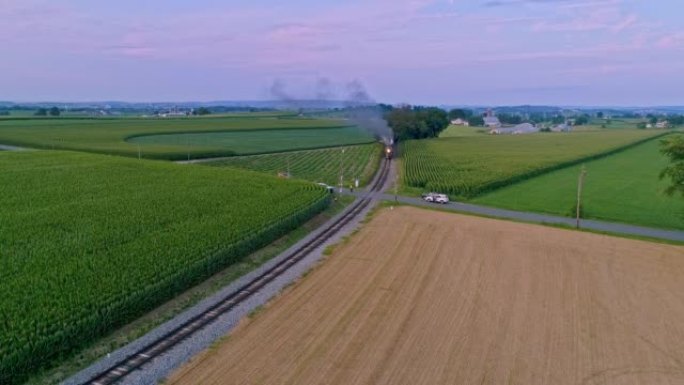 一列蒸汽火车的鸟瞰图正驶过农田和玉米田，吹着浓烟。