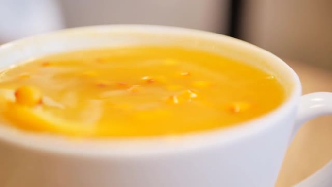极端特写勺子在大杯子里搅拌橙子沙棘茶