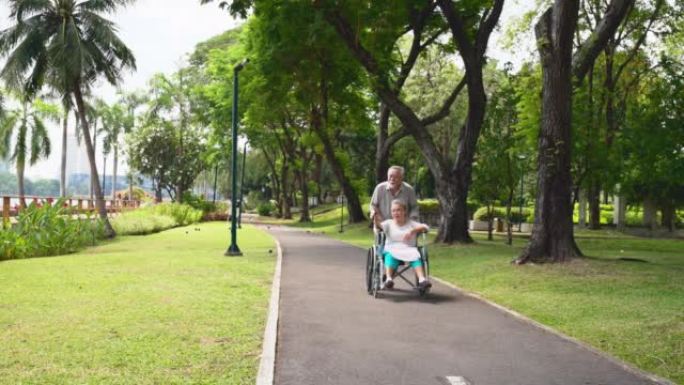 年迈的丈夫将妻子的轮椅推下公园的人行道。