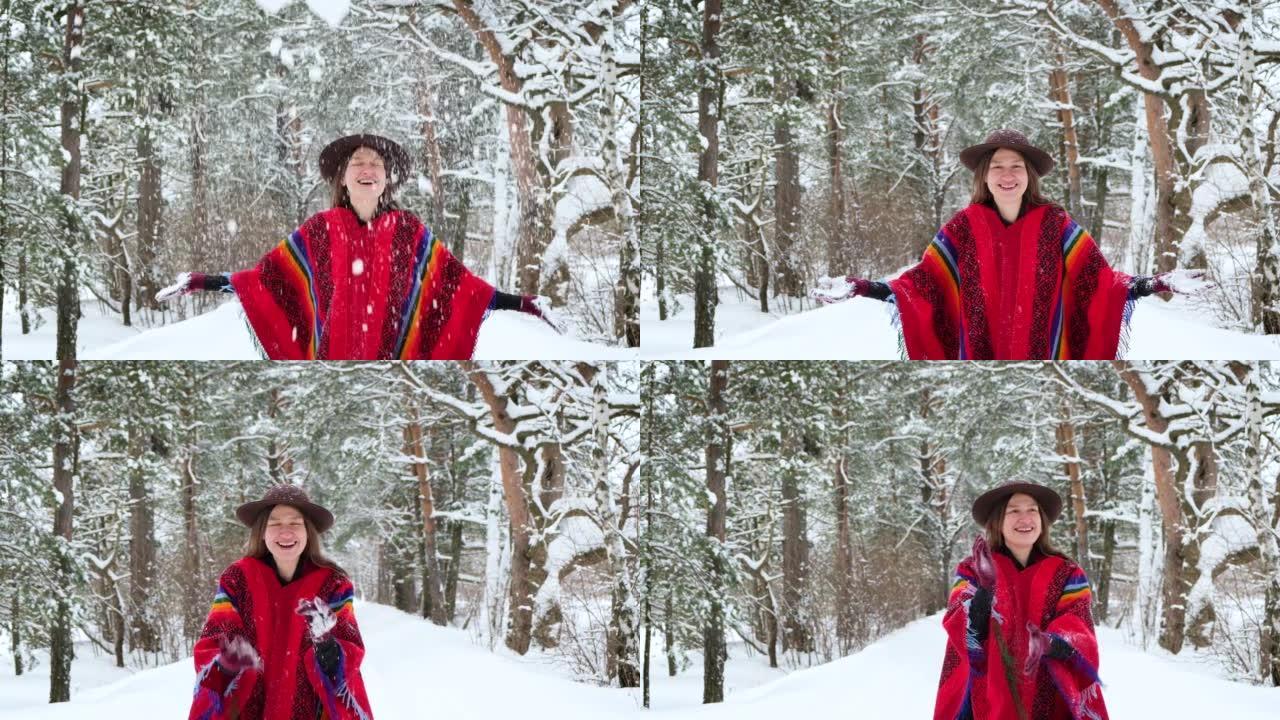 快乐女人的户外肖像穿着彩色波西米亚风格的民族羊毛雨披和毡帽在森林里扔雪。享受冬天的快乐。