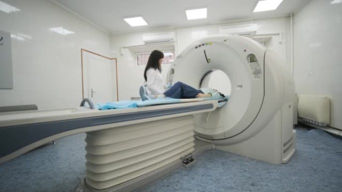 戴口罩的女性患者正在现代医疗诊所接受CT或MRI扫描。患者躺在CT或MRI扫描台上，进入机器