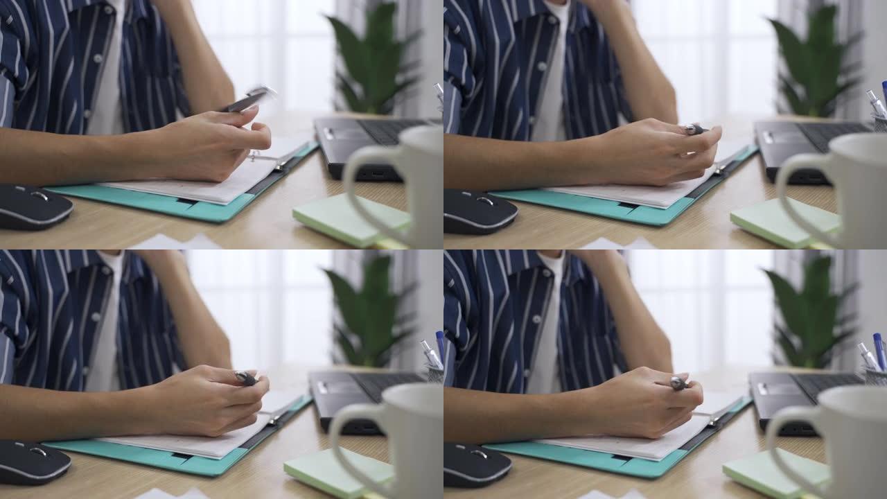 特写镜头拍摄了一个男人的手放在办公桌上，笔记本电脑和电脑正在旋转一支笔，同时在明亮的家庭室内思考一些