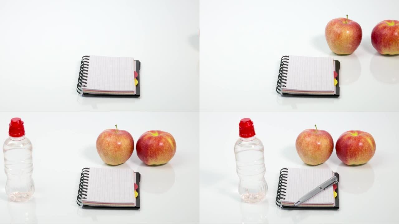 两个红色成熟的苹果，一瓶水，一支笔和一个笔记本
