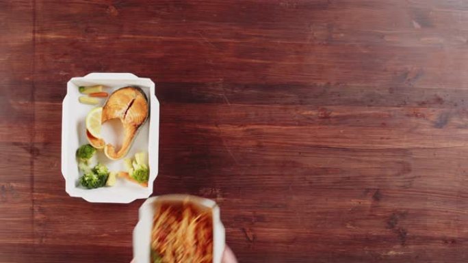 送餐俯视图，在木制桌子上的一次性容器中带走餐点。午餐盒，配有煮熟的蔬菜沙拉，意大利肉酱和鲑鱼鱼。健康