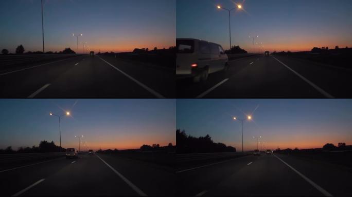 黄昏日落路灯。晚上，摄像头在前面，挡风玻璃参考。在黑暗的高速公路上驾驶汽车。日落之后，晚上在高速公路