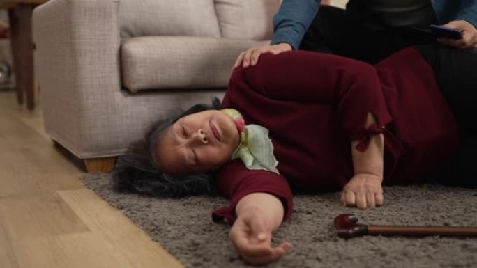 昏迷的亚洲高级女祖母躺在地板上的特写镜头，家人的手在摇晃她的身体，试图唤醒她。老年人跌倒和居家淡淡的