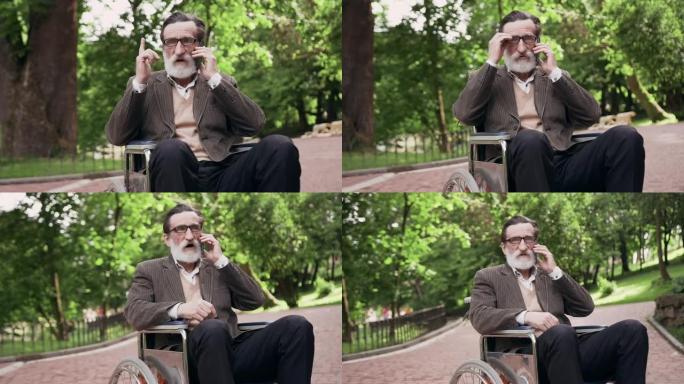 可爱的受人尊敬的戴眼镜的大胡子老人坐在城市公园的轮椅上，在手机上聊天，前视图