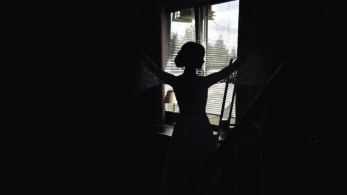一个穿着裙子的女孩的剪影，她举起双手站在窗户的背景下。