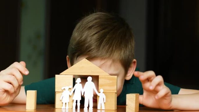 7岁的白人男孩玩木方块盖房子，孩子从纸上剪出一个家庭。家庭梦想。儿童对家庭和家庭的积极梦想