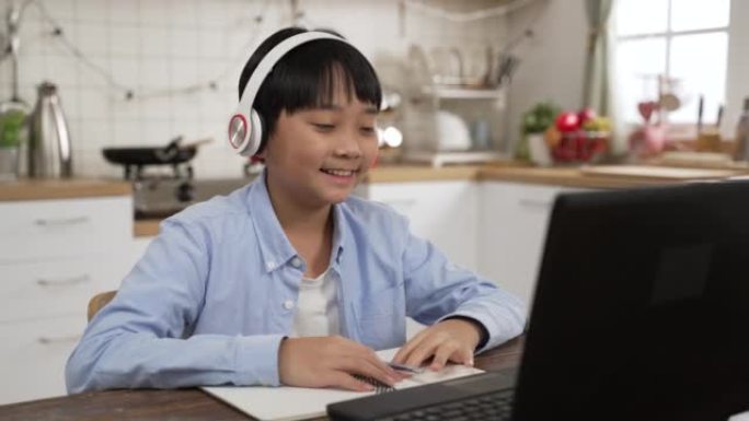 亚洲男学生在线学习班在线学习视频，快乐男孩挥动双手，在家用笔记本电脑在线学习英语。新型冠状病毒肺炎冠