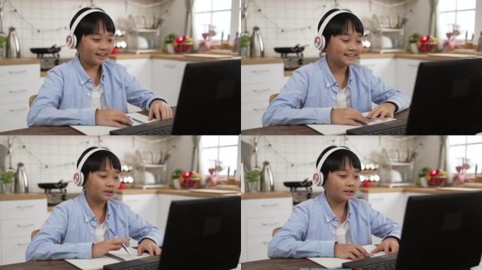 亚洲男学生在线学习班在线学习视频，快乐男孩挥动双手，在家用笔记本电脑在线学习英语。新型冠状病毒肺炎冠