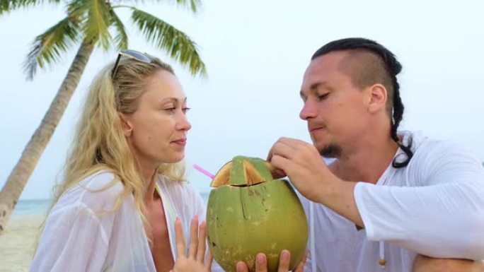 性感的情侣在棕榈树下亲吻、拥抱和喝椰子鸡尾酒Pina Colada。概念蜜月关系浪漫海滩热带旅游，夏