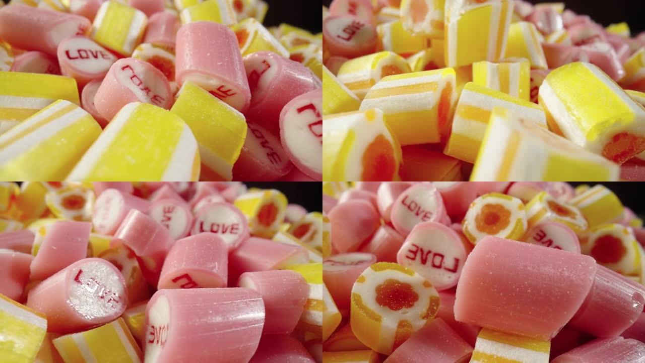 彩色条纹焦糖糖果，黑色背景上的铭文爱情旋转。粉色和黄色棒棒糖的混合特写。糖果店。节日或儿童生日的节日