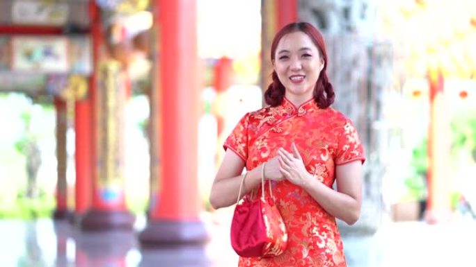 穿着红色旗袍的年轻亚洲美女的肖像，对着镜头微笑，做着中国人的问候手势。美丽快乐的女孩在做祝贺的手势。