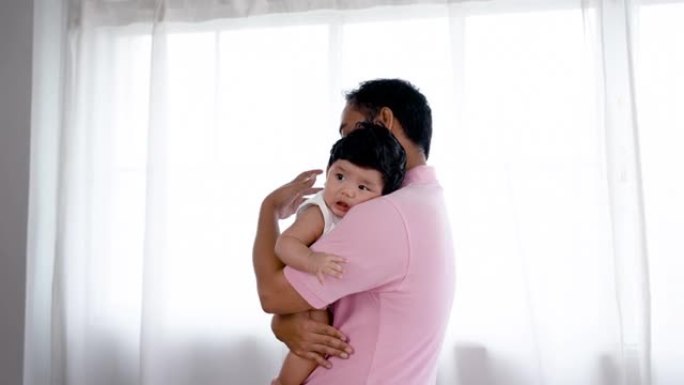 4K 25fps慢动作，亚洲父亲抱着可爱的新生儿子慢慢地走路，抚摸婴儿的背部，在卧室里，家人健康 .