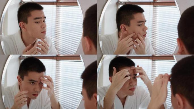 不快乐的亚洲男人挤粉刺在浴室里看着镜子