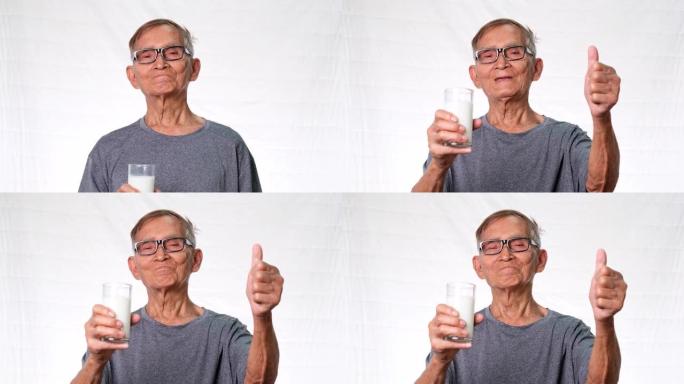 在工作室里，健康的老人拿着一杯牛奶，在白色背景上竖起大拇指。