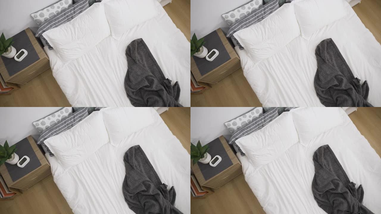 顶角视图，早上在现代明亮的卧室内部，放大白色未整理的凌乱床，配有毯子和枕头。