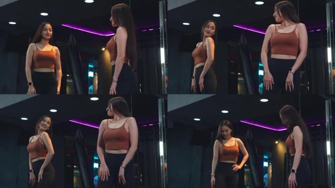 健身房里的一名亚洲女性，在健身一小时后，她自豪而自信地站在镜子前看着自己的身体。
