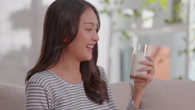 健康年轻的亚洲女性在家中喝钙牛奶，强壮的骨骼，微笑的印度女性在玻璃上拿着豆浆享受营养健康生活，天然牛
